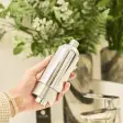 Hånd der holder et cylinderformet brusefilter i blank krom foran grønne planter