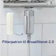 Hvid filterpatron ved siden af et filterhus i krom monteret under en armatur, med en pil der viser hvor patronen skal sidde