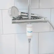 Håndbruser i krom med rundt brusehoved på en termostatarmatur, med et hvidt Brusefilteret-filter monteret mellem armatur og bruseslange