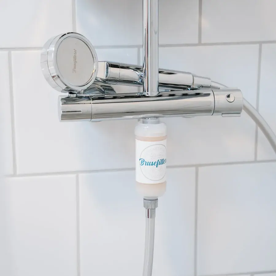 Håndbruser i krom med rundt brusehoved på en termostatarmatur, med et hvidt Brusefilteret-filter monteret mellem armatur og bruseslange