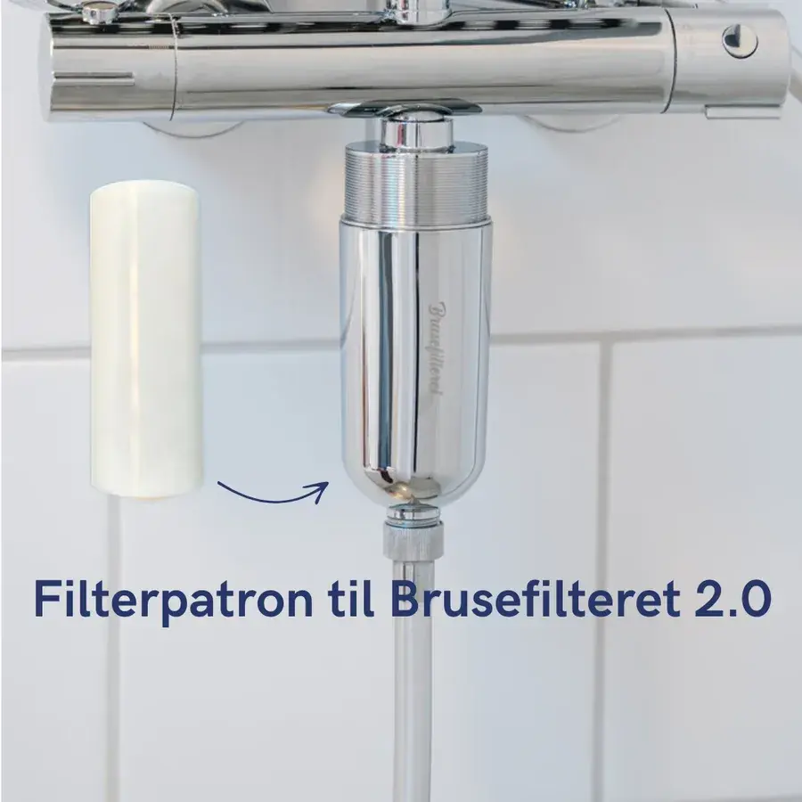 Hvid filterpatron ved siden af et filterhus i krom monteret under en armatur, med en pil der viser hvor patronen skal sidde